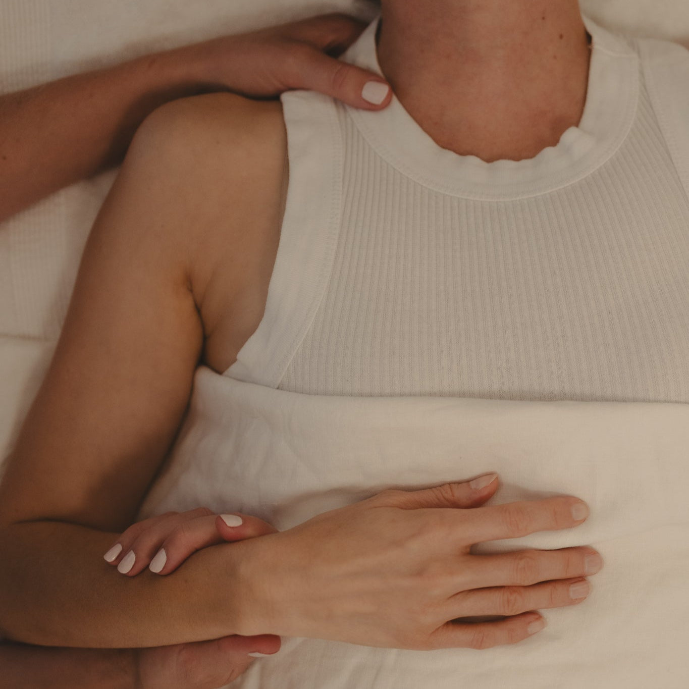 Close-up of a person receiving Jin Shin Jyutsu wearing a white sleeveless top with another arm resting on their shoulder.